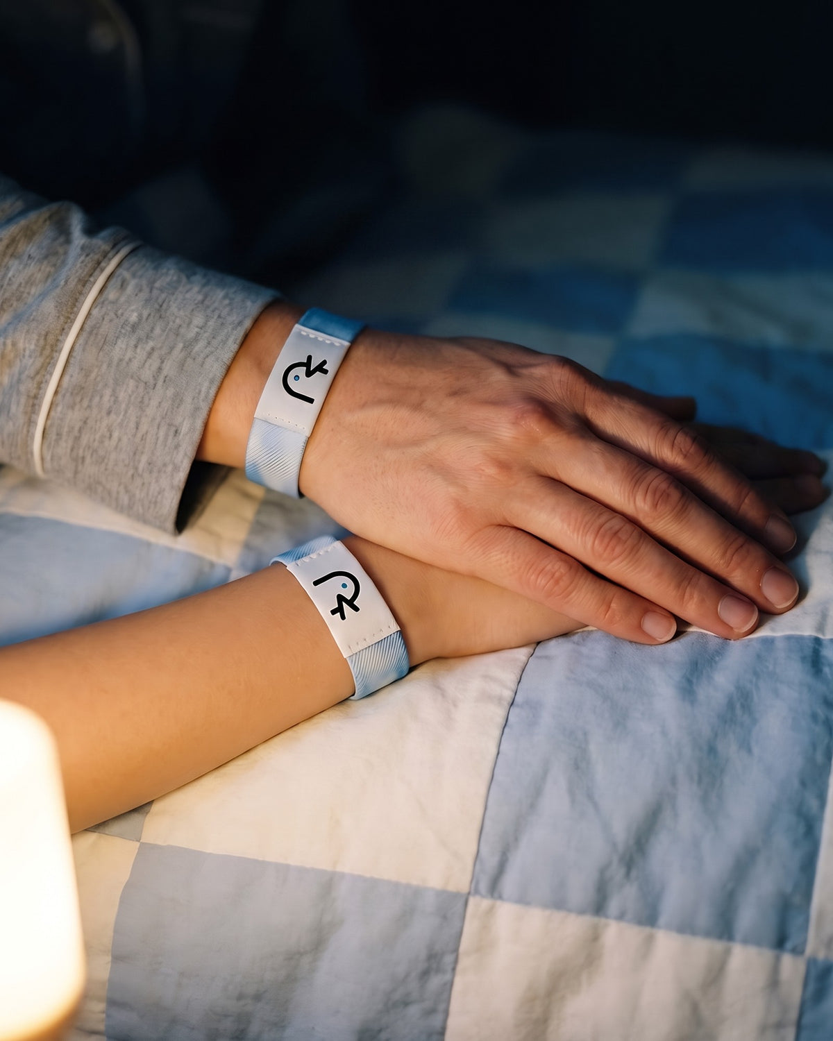 A mother’s hand resting on her daughter’s hand on a quilt at night, both wearing the sky-blue Faith Over Fear band