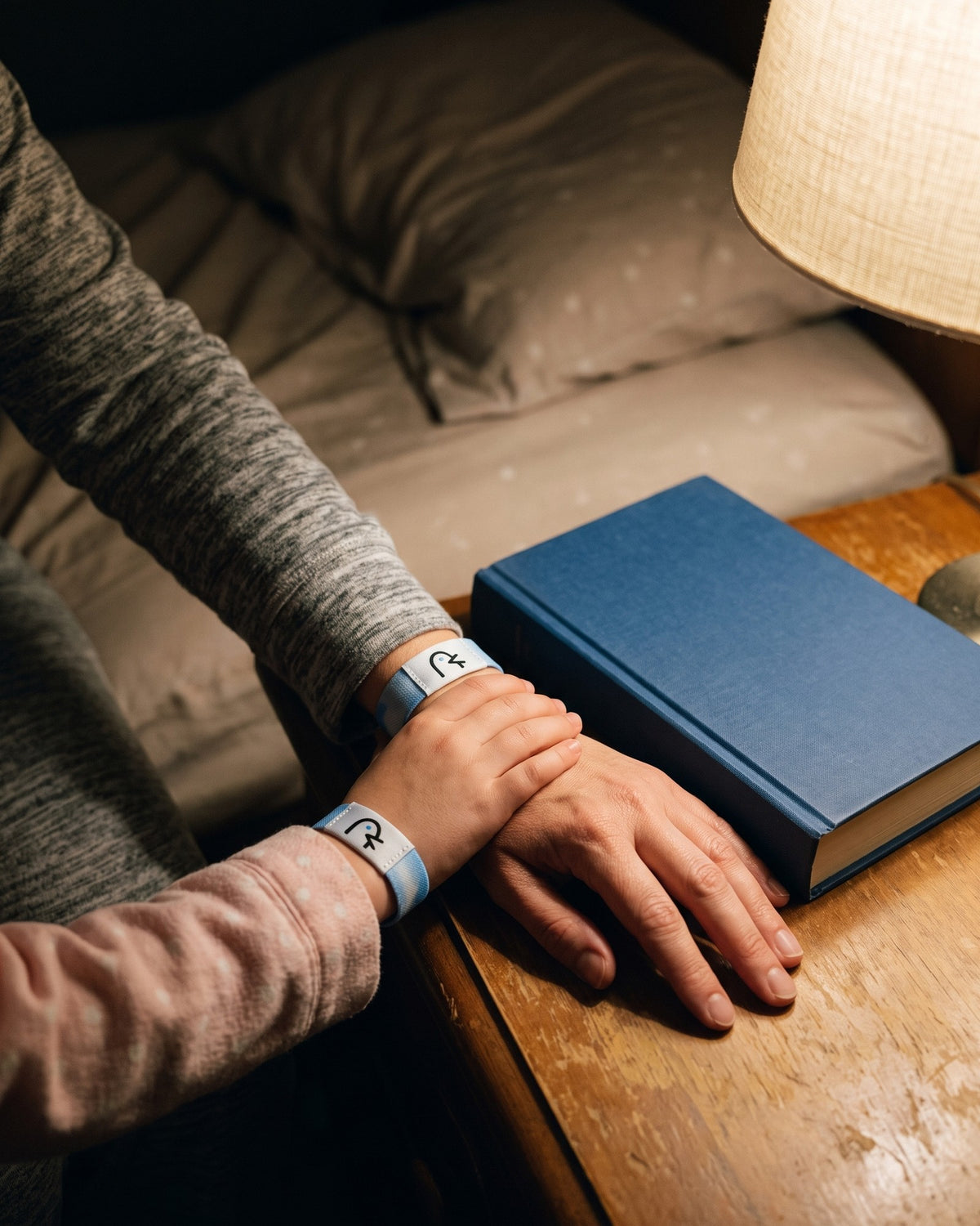 A daughter’s small hand resting on her mother’s hand on a nightstand under a lamp, both wearing Faith Over Fear bands