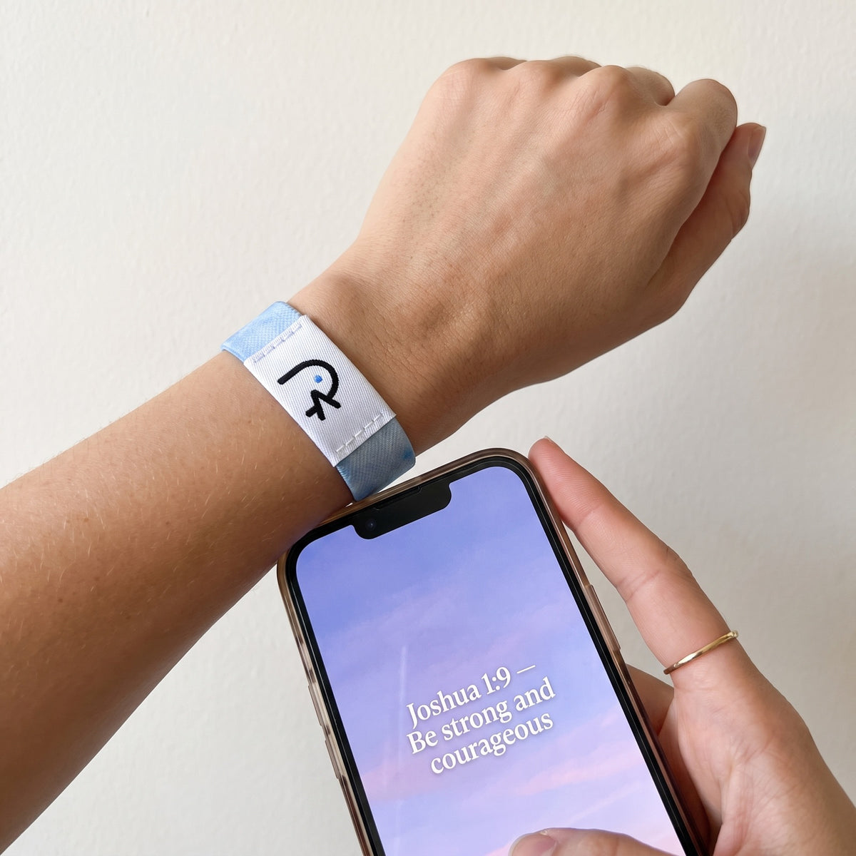 A phone held to the white label of a sky-blue Faith Over Fear band, a Bible verse on the screen