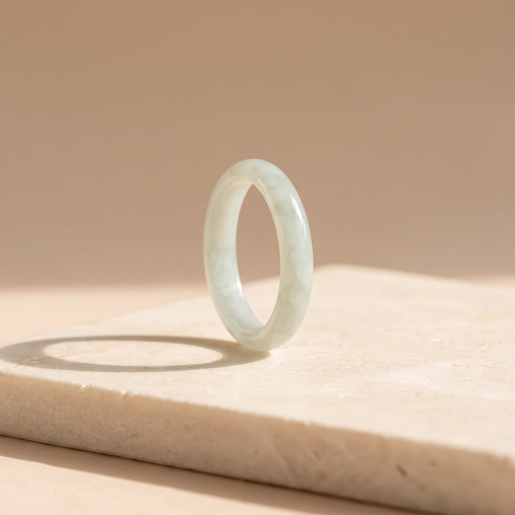 Jade Stacking Ring – slim pale green jade band standing on a cream stone slab in soft daylight